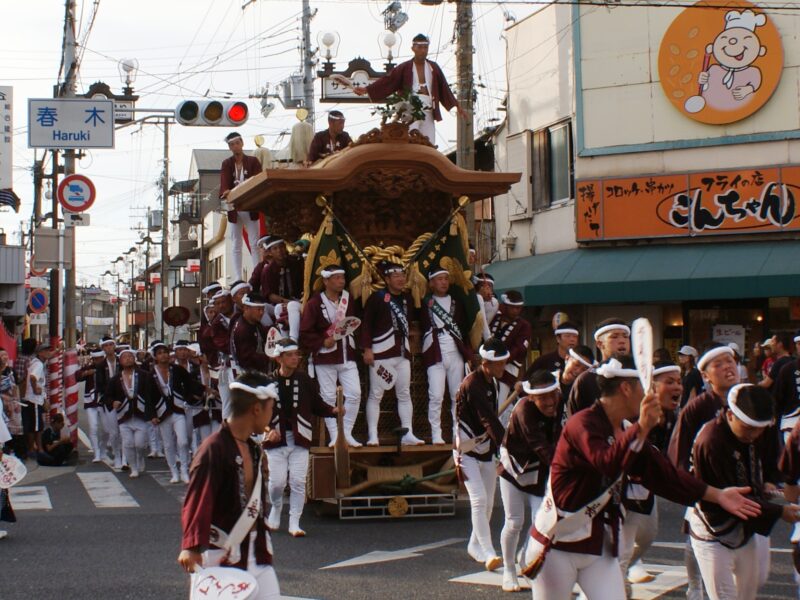 Participants in maroon jackets accompany a carved wooden float through Haruki in Kishiwada, Osaka Prefecture, during a neighborhood danjiri procession.