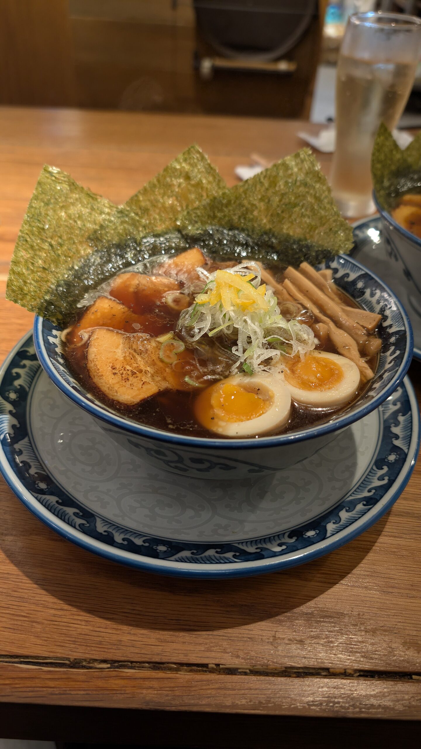 Ramen in a patterned bowl in Osaka is topped with pork, soft egg halves, bamboo shoots, scallions and upright seaweed sheets.