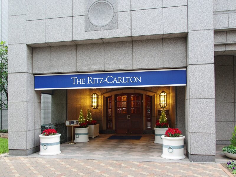 The Ritz-Carlton Osaka entrance has wooden doors, warm lanterns and flower planters beneath a blue hotel sign.