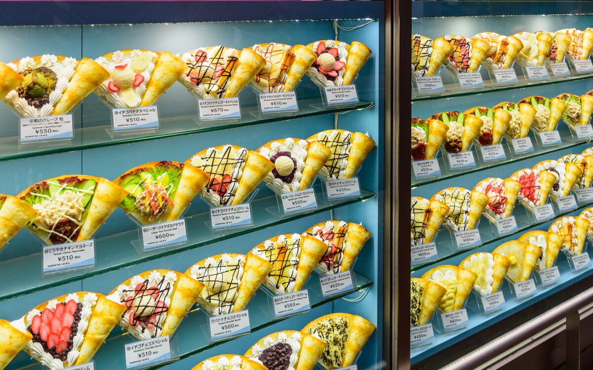 Rows of plastic crepe samples with fruit, cream and colorful toppings fill a glass display case in Dotonbori, Osaka.