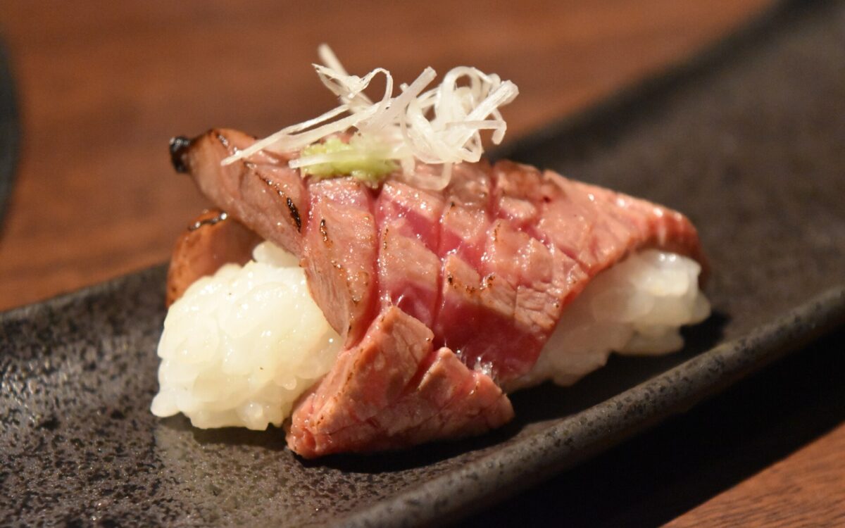 Seared Matsusaka beef slices cover two portions of sushi rice on a dark rectangular plate in Osaka.