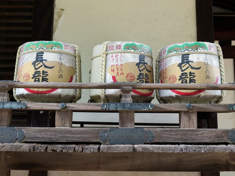Three straw-wrapped sake barrels sit behind a wooden railing at Domyoji Tenmangu shrine in Fujiidera, Osaka Prefecture.