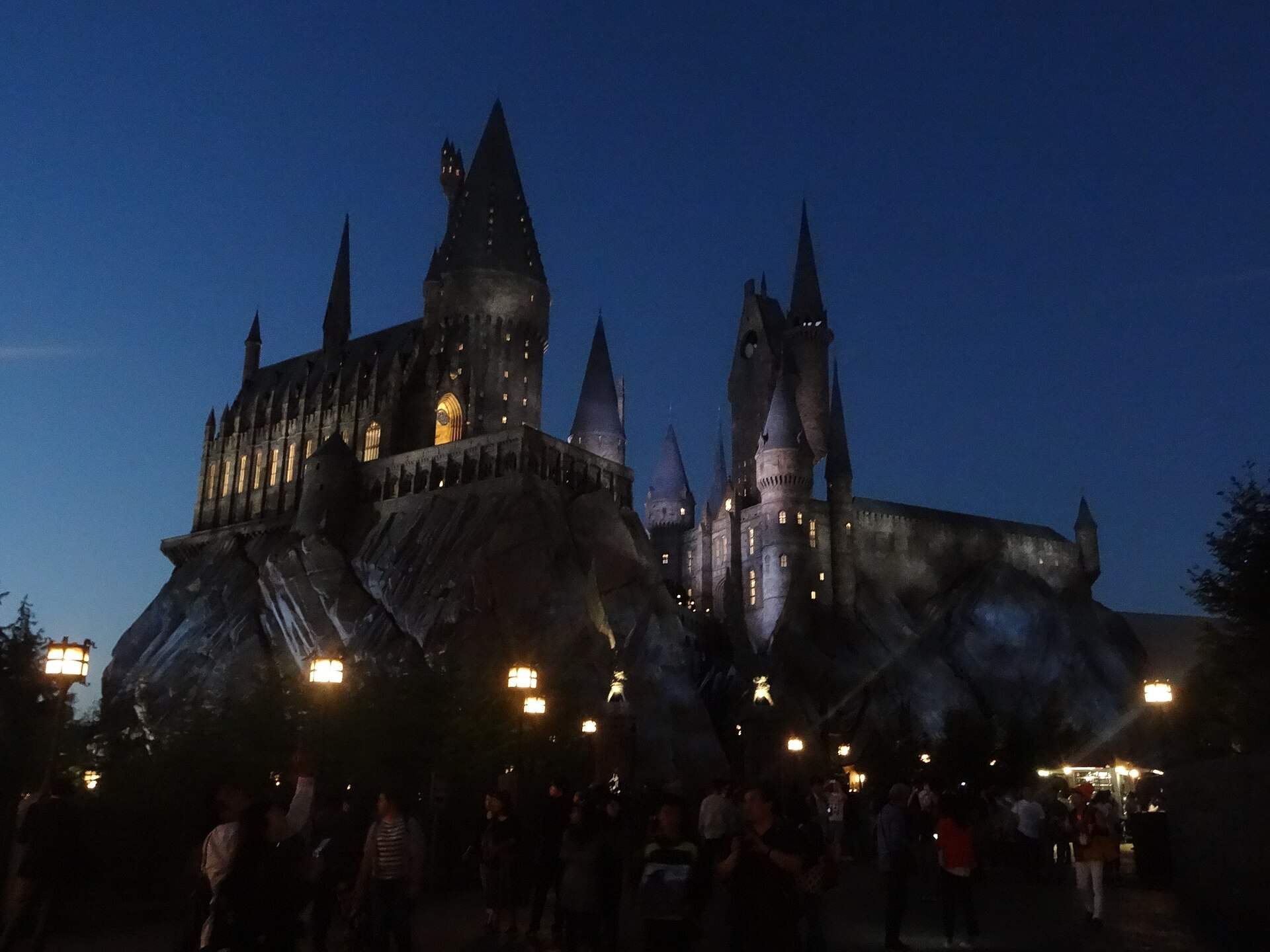 Hogwarts Castle at Universal Studios Japan silhouetted against a deep blue dusk sky, with lamps lit along the path below