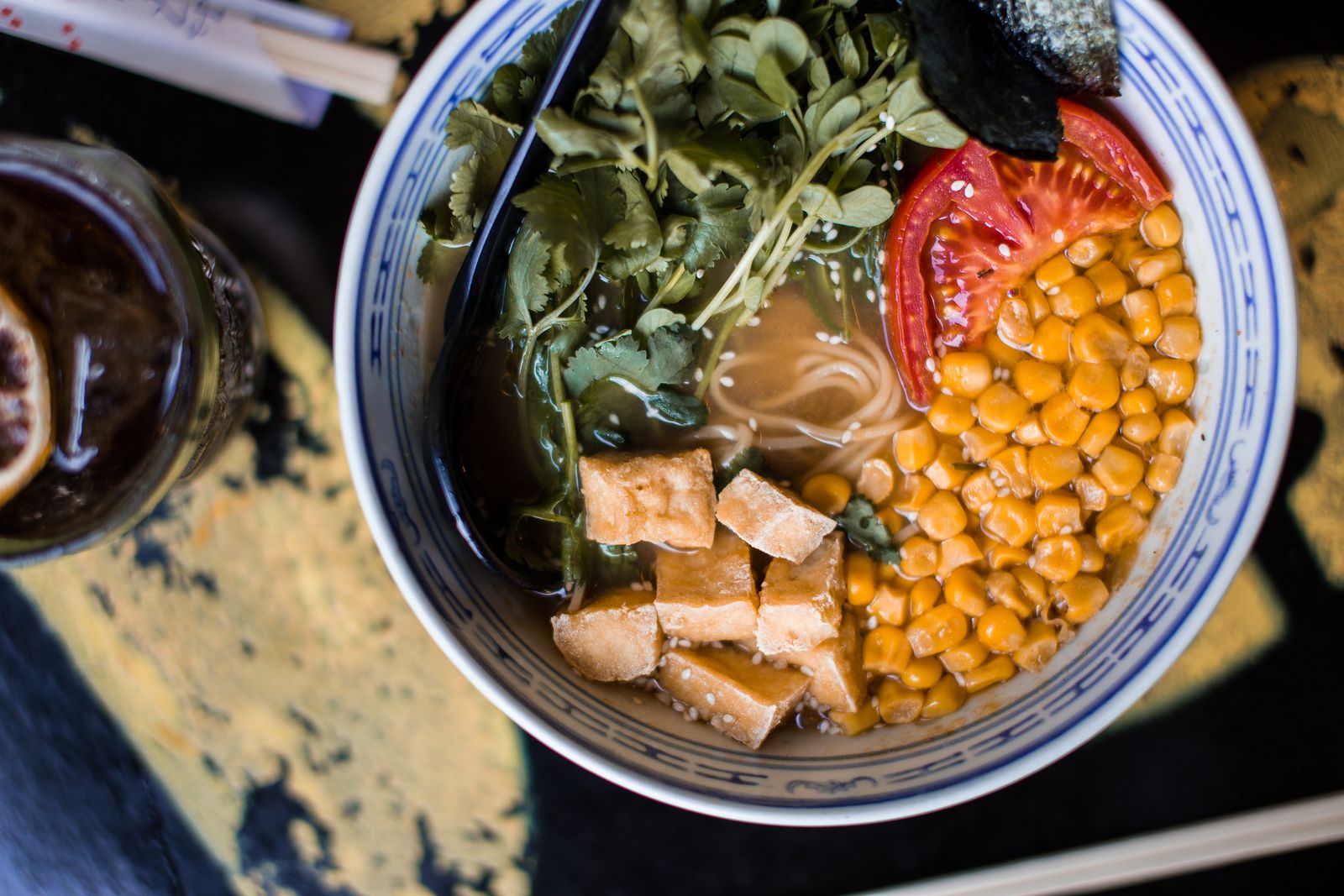 A plant-based ramen with cubes of fried tofu, sweetcorn, tomato and fresh greens in a blue-and-white bowl