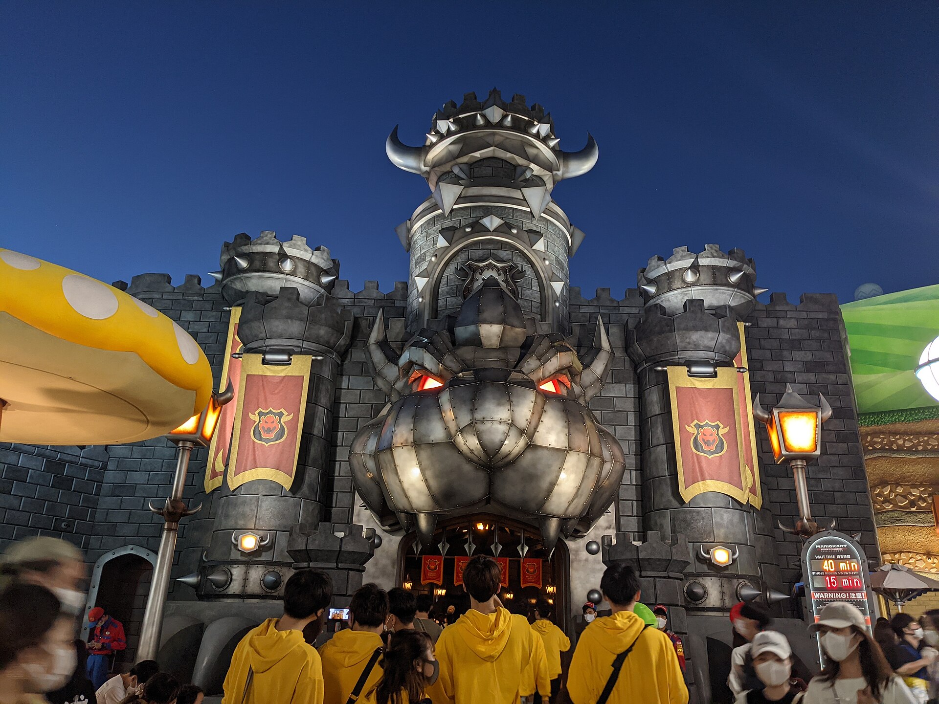 Visitors gather beneath the giant Bowser head at Bowser's Castle in Super Nintendo World, Universal Studios Japan, Osaka, at dusk.