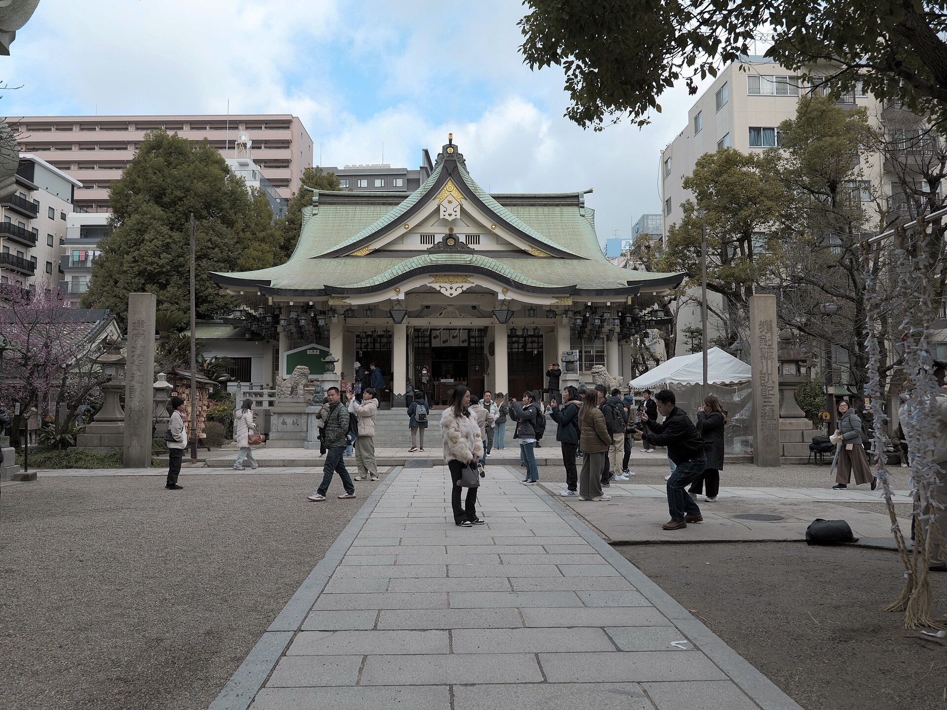 Visitors stand along the stone approach to Namba Yasaka Shrine's worship hall, beneath curved green roofs in Osaka.